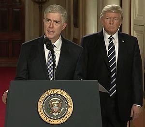 Neil Gorsuch standing at podium with Donald Trump behind him