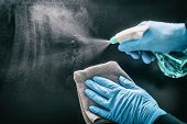 Person cleaning surface with blue gloves and spray